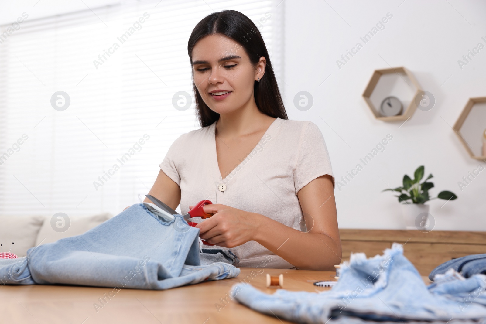 Photo of Young woman cutting jeans with scissors at wooden table indoors