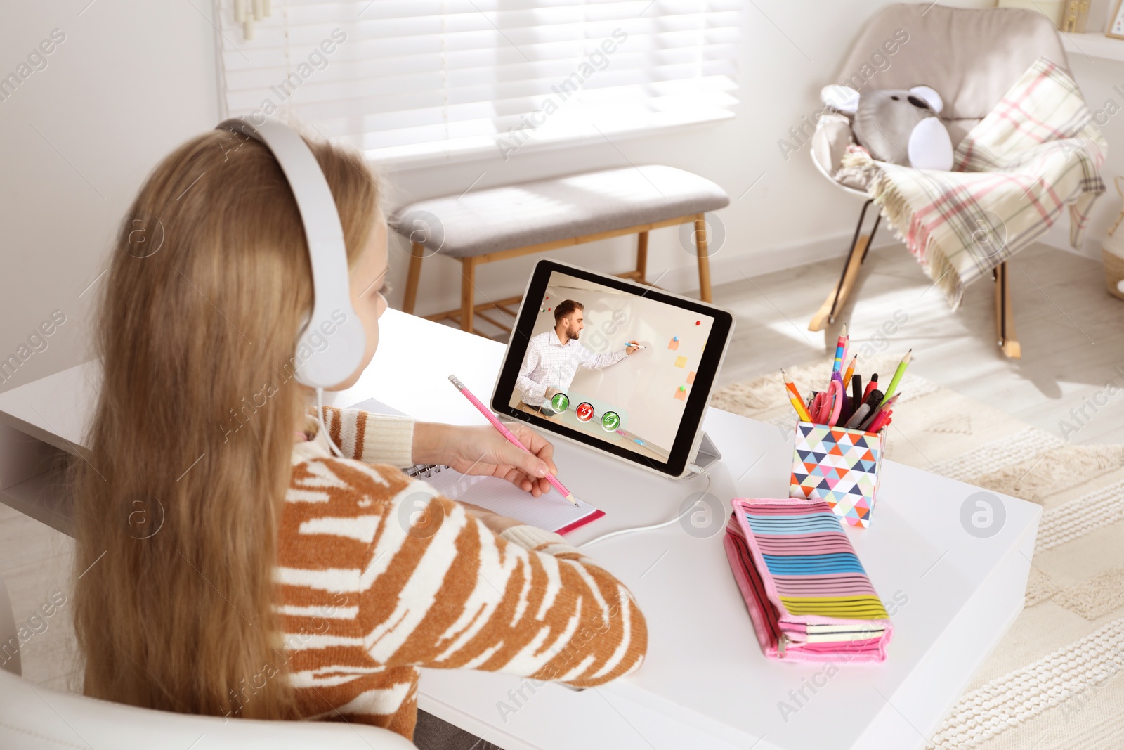 Image of E-learning. Little girl taking notes during online lesson at table indoors