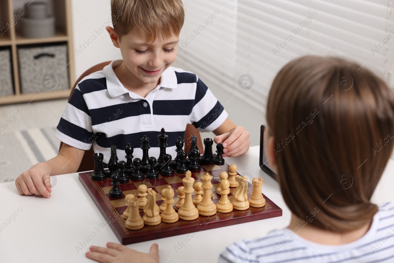 Photo of Cute children playing chess at table in room