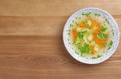 Bowl of fresh homemade soup to cure flu on wooden background, top view with space for text