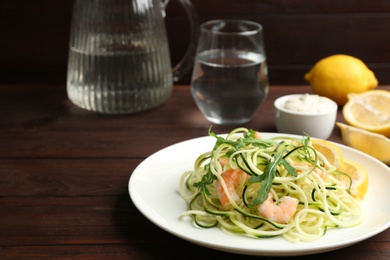 Photo of Delicious zucchini pasta with arugula and shrimps served on wooden table. Space for text