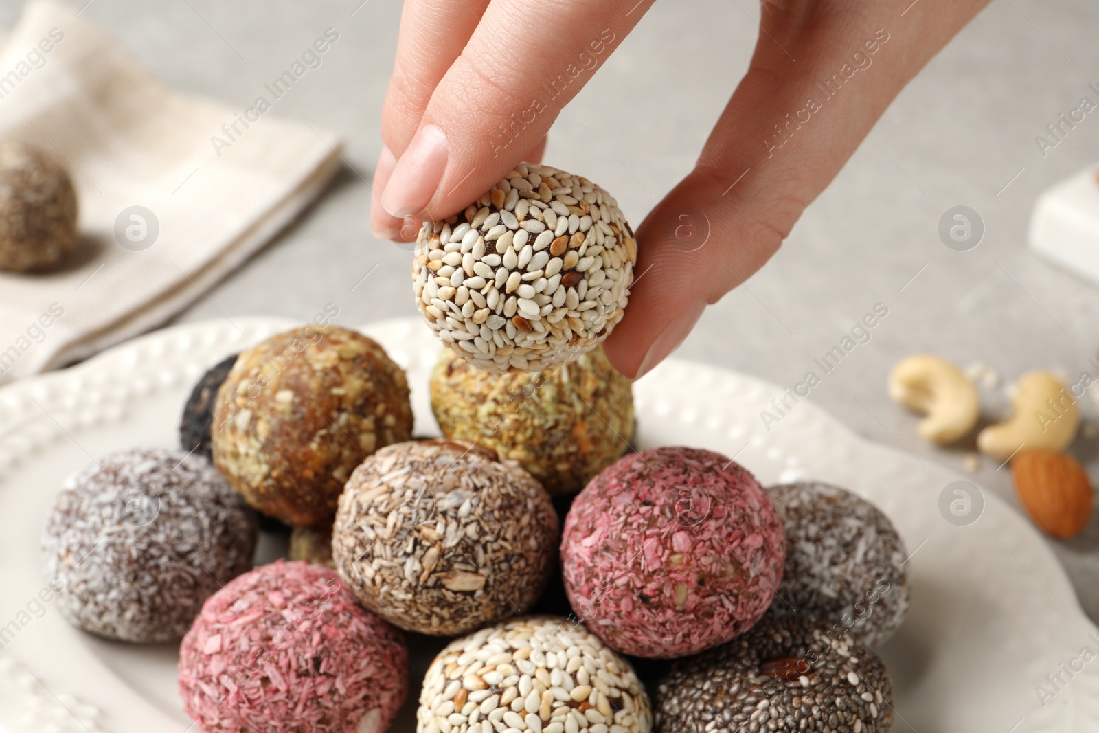 Photo of Woman taking delicious vegan candy ball from plate at table, closeup