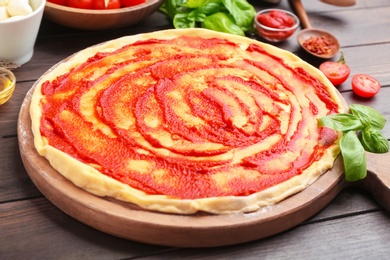 Photo of Raw dough for pizza with red sauce on wooden table