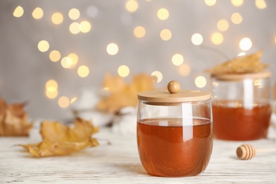 Photo of Glass jars with sweet honey on table against blurred lights. Space for text