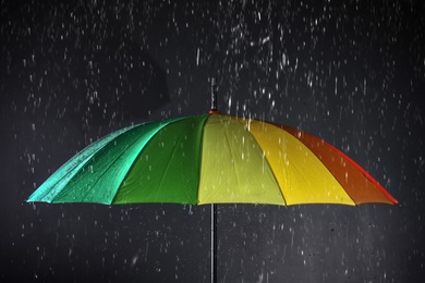 Photo of Bright umbrella under rain on dark background