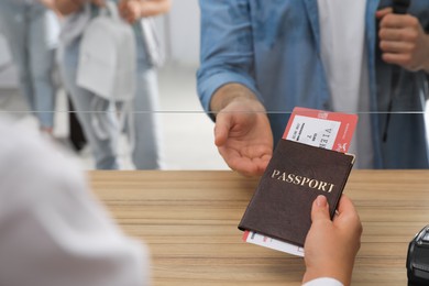 Photo of Agent giving passport with ticket to client at check-in desk in airport, closeup