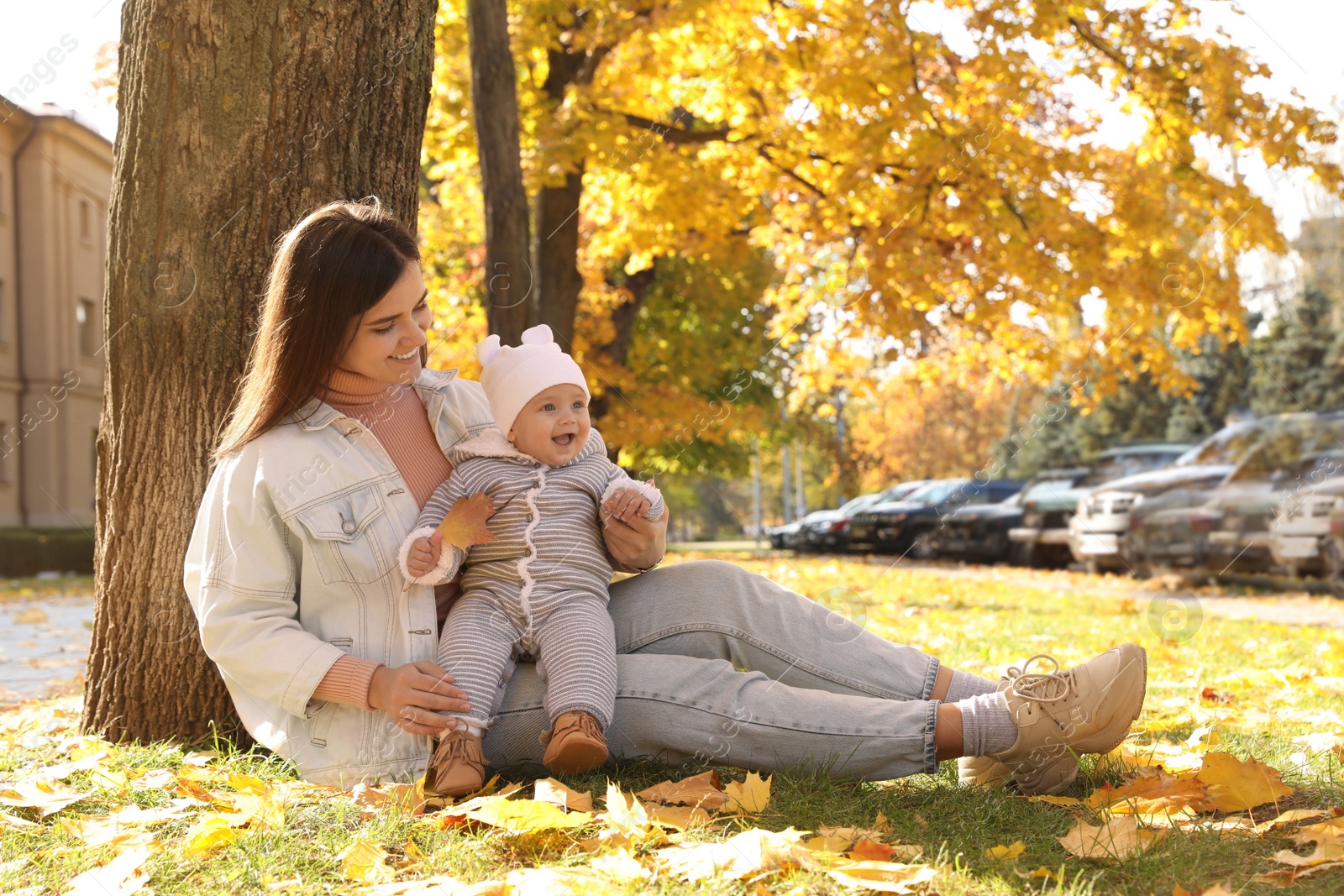 Photo of Happy mother with her baby daughter sitting near tree in park on sunny autumn day, space for text