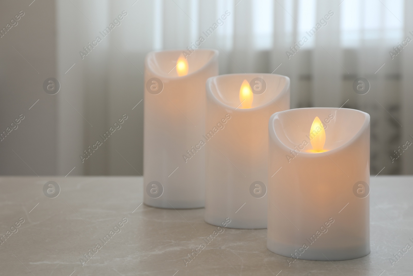 Photo of Glowing decorative LED candles on grey table. Space for text