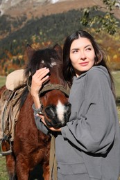 Young woman hugging horse in mountains on sunny day. Beautiful pet