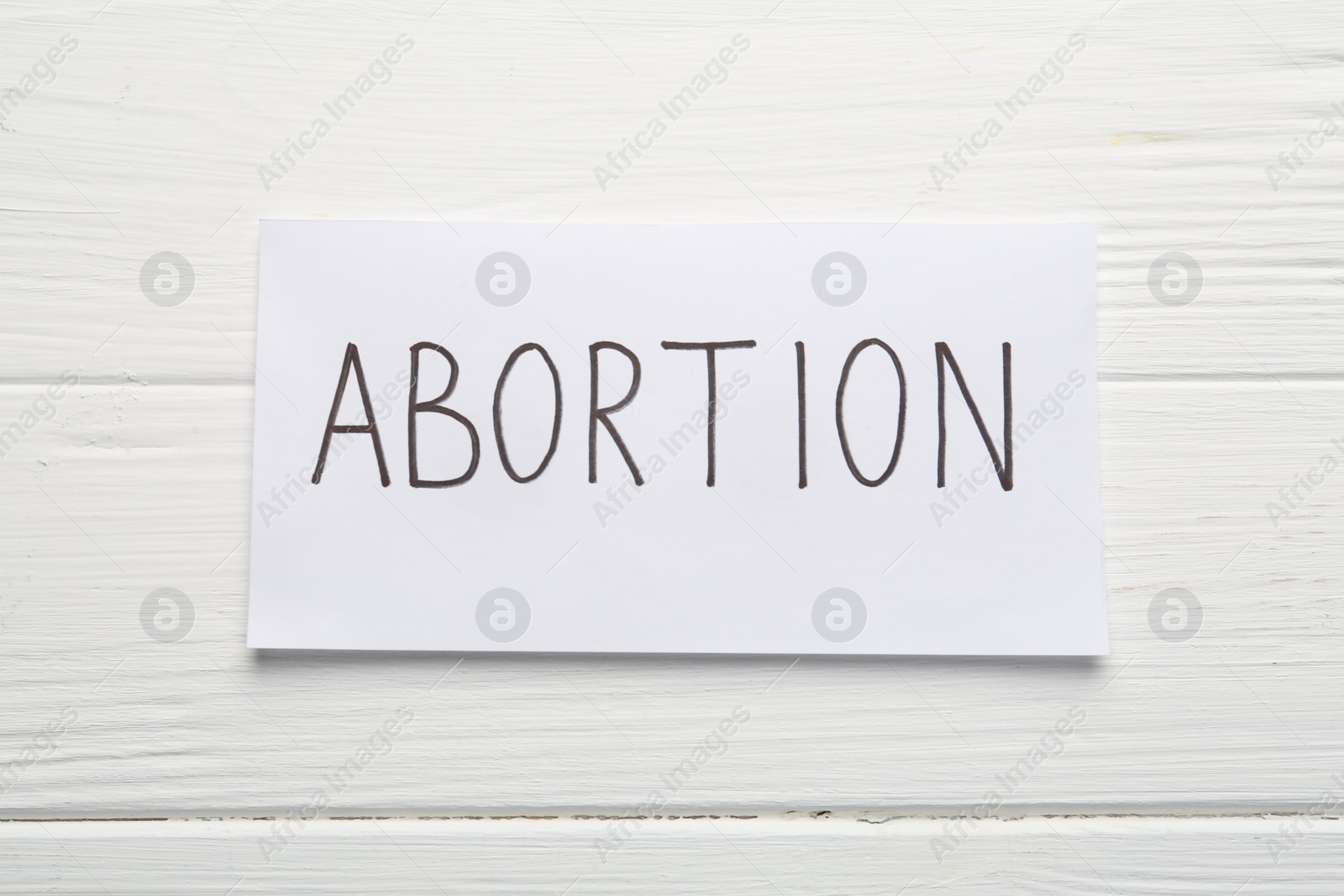 Photo of Paper note with word Abortion on white wooden background, top view