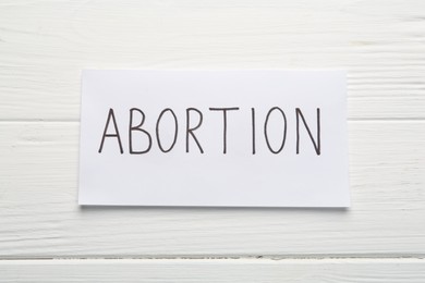 Photo of Paper note with word Abortion on white wooden background, top view