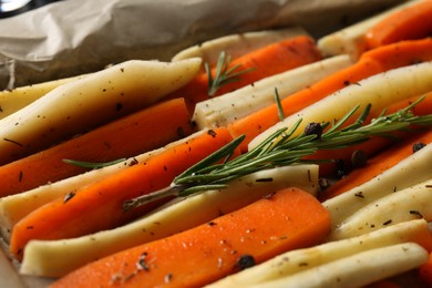 Slices of parsnip and carrot with rosemary on baking tray, closeup