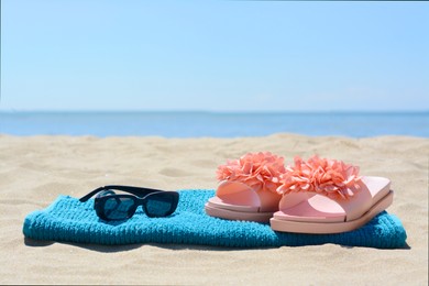 Photo of Towel, flip flops and sunglasses on sand near sea. Beach accessories