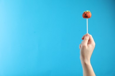 Woman with delicious pumpkin shaped cake pop and space for text on light blue background, closeup. Halloween celebration