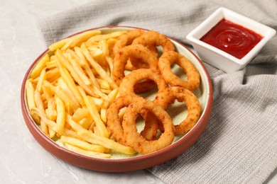 Photo of Tasty ketchup with fries and onion rings on light grey table, closeup