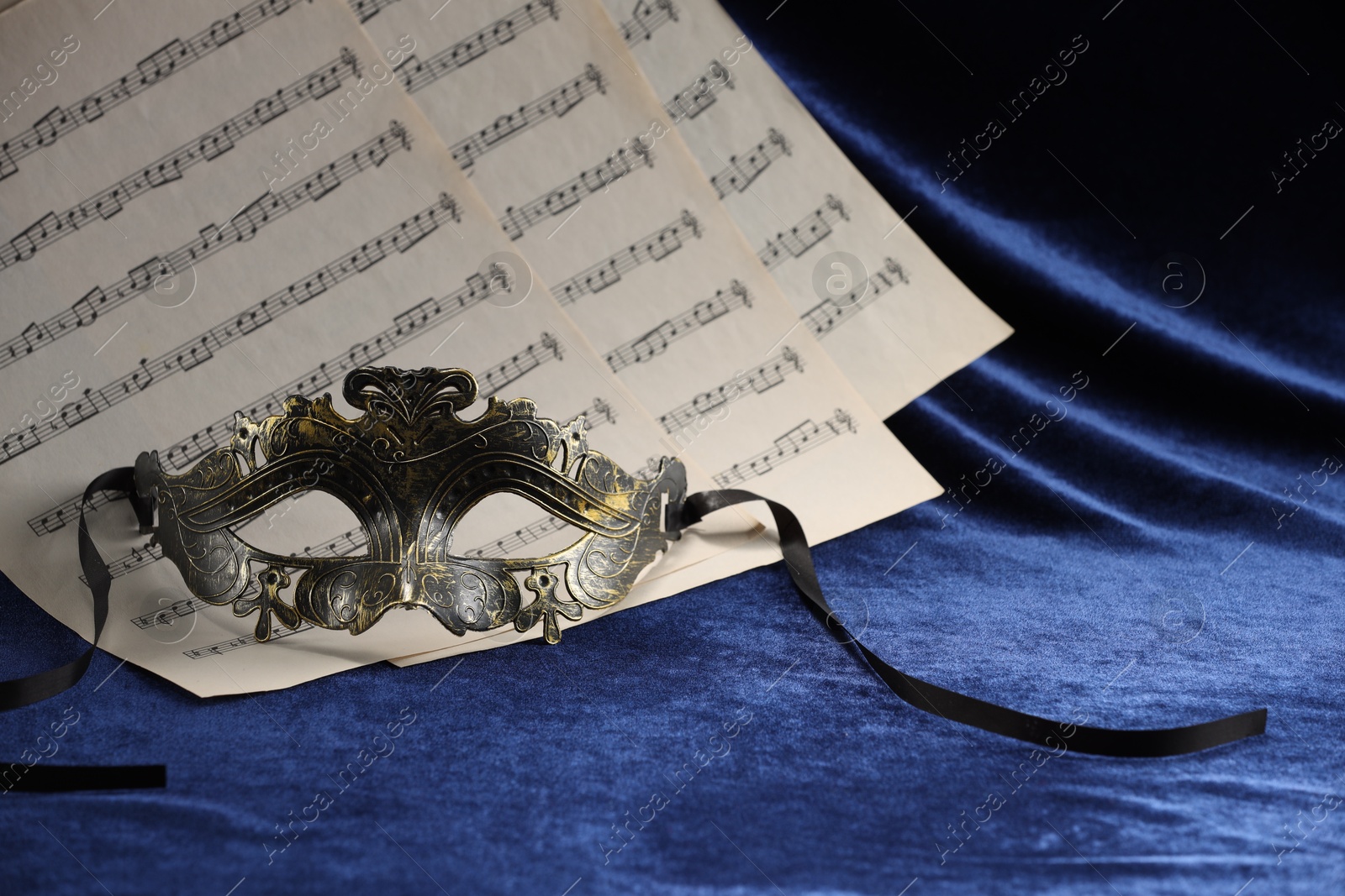 Photo of Elegant face mask and music sheets on blue fabric. Theatrical performance