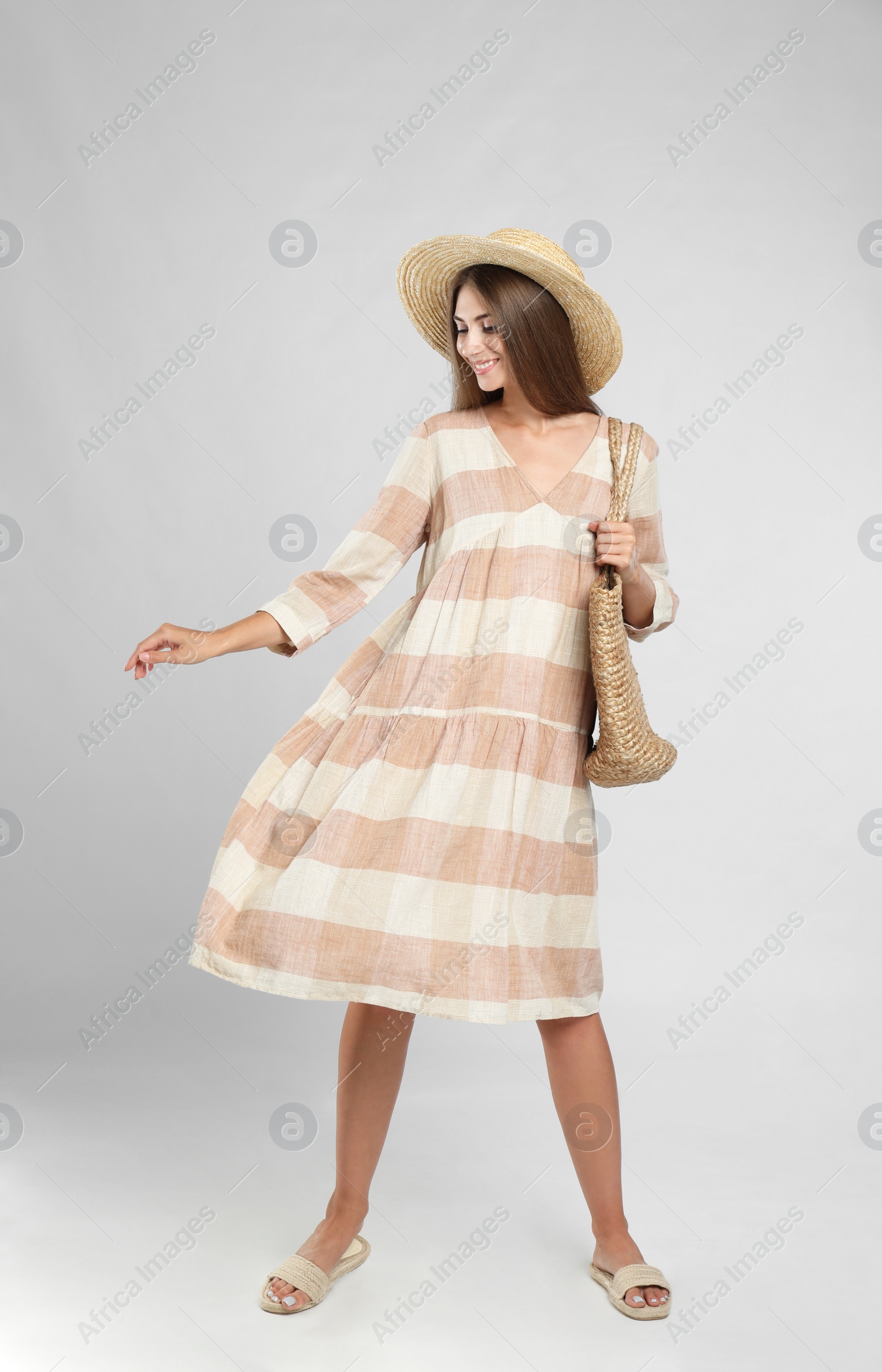 Photo of Young woman wearing stylish dress with straw bag on light grey background