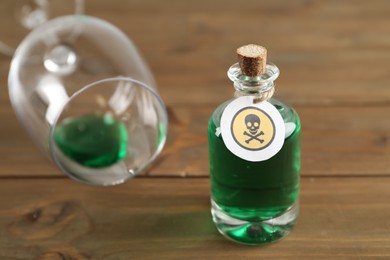 Photo of Bottle of poison and partially emptied glass on wooden table