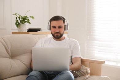 Photo of Man with laptop and headphones sitting on sofa at home