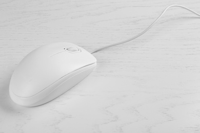 Photo of Modern wired optical mouse on white wooden table. Space for text