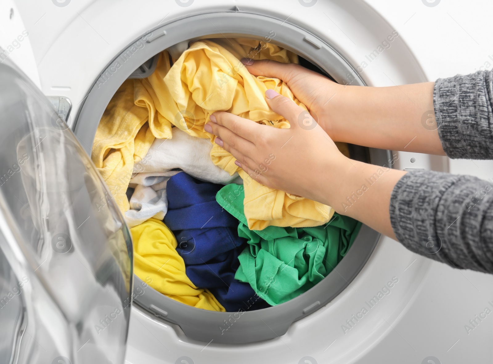Photo of Young woman putting clothes into washing machine, closeup