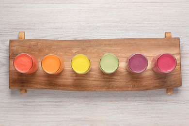 Photo of Board with many different tasty smoothies on white wooden table, top view