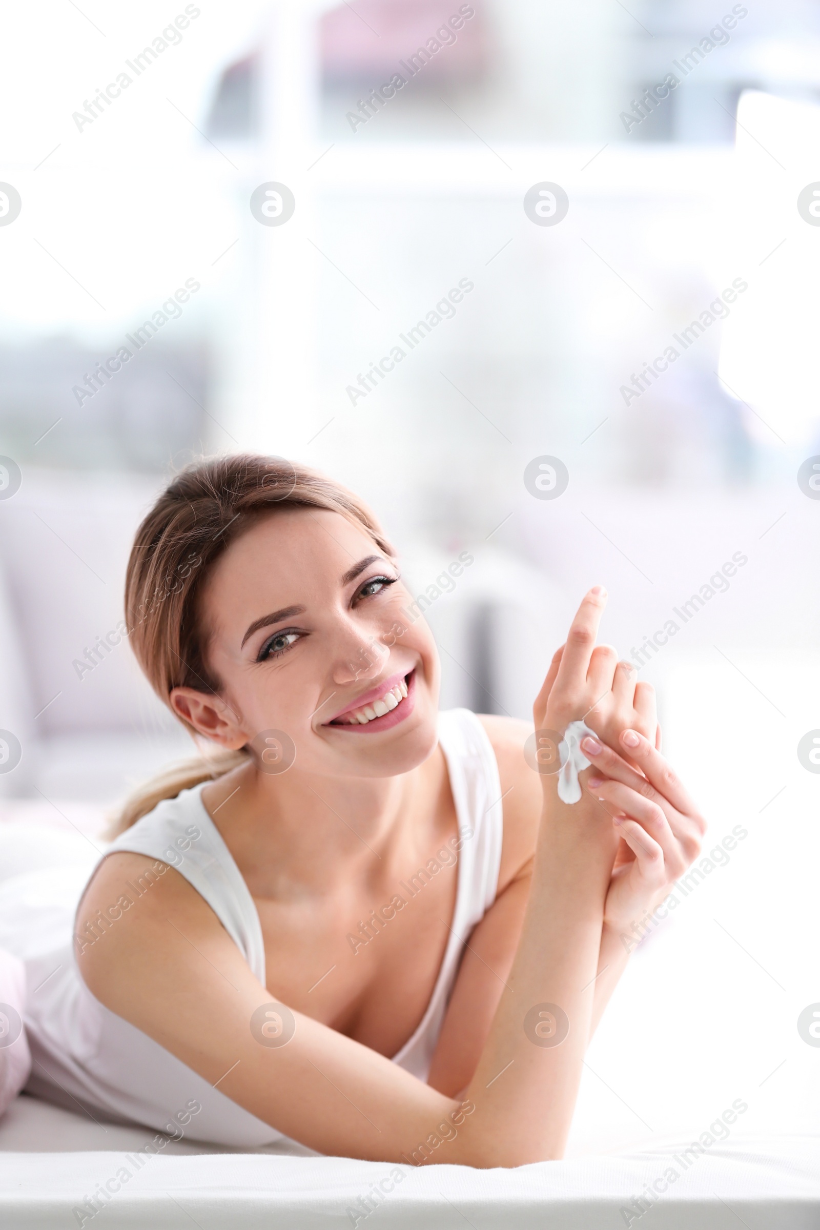 Photo of Young woman applying hand cream on bed at home