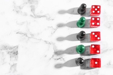 Red dices and game pieces on white marble table, flat lay. Space for text