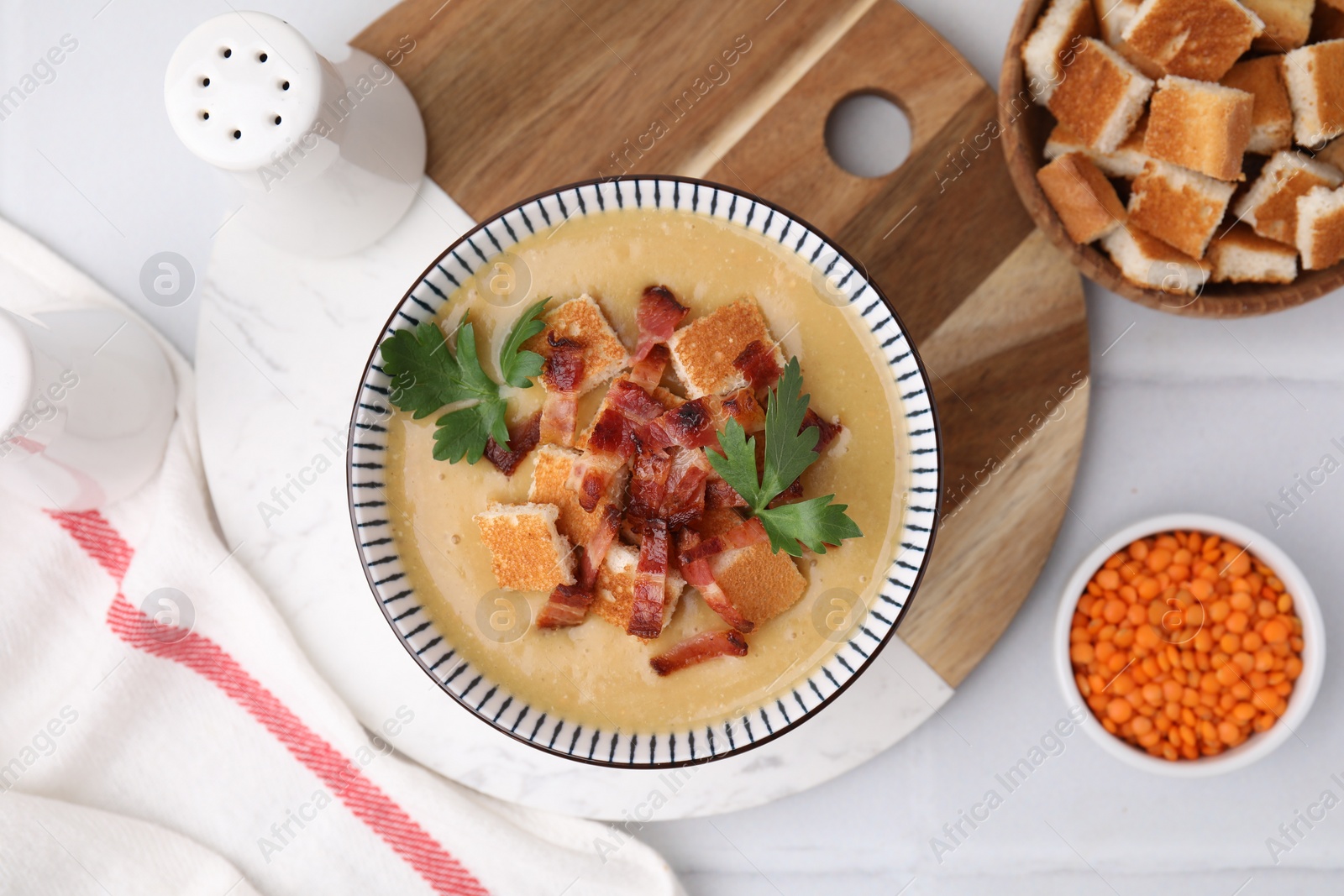 Photo of Delicious lentil soup with bacon and parsley in bowl on white table, flat lay