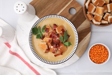 Delicious lentil soup with bacon and parsley in bowl on white table, flat lay