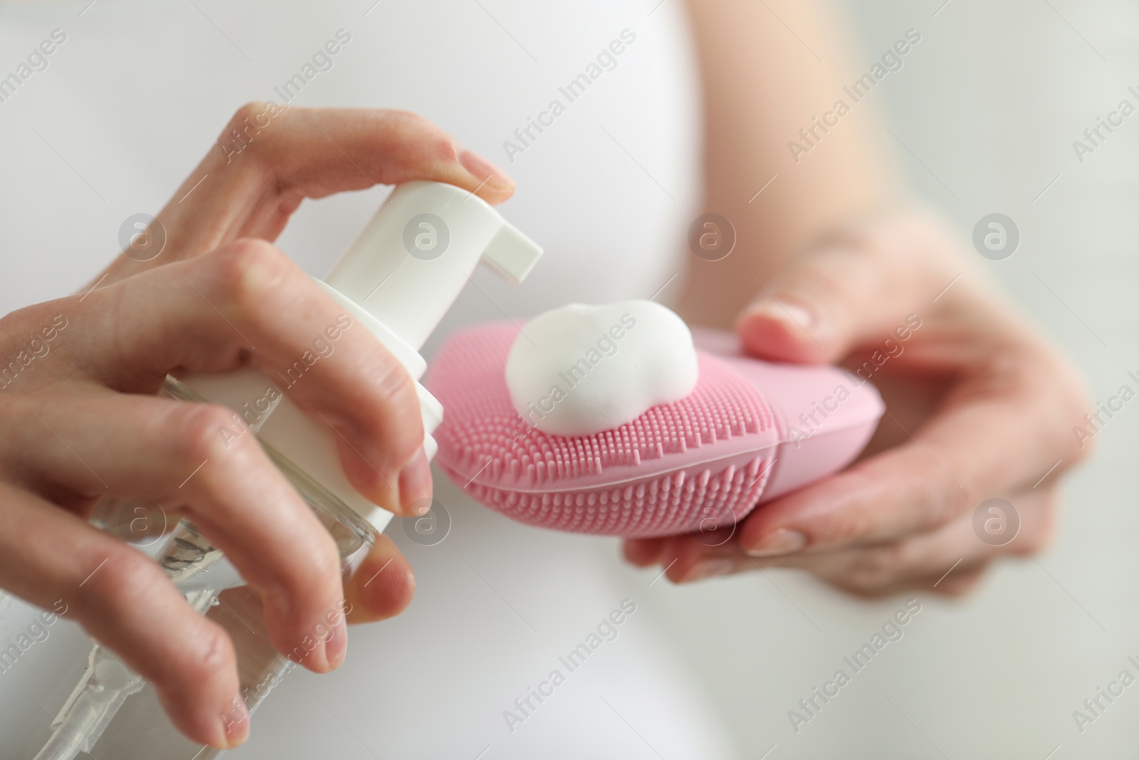 Photo of Washing face. Woman applying cleansing foam onto brush against light background, closeup