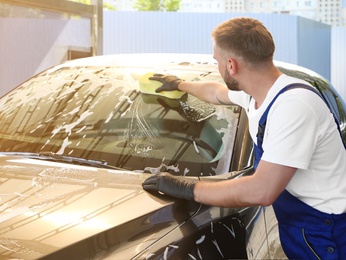 Photo of Young worker cleaning automobile with sponge at car wash