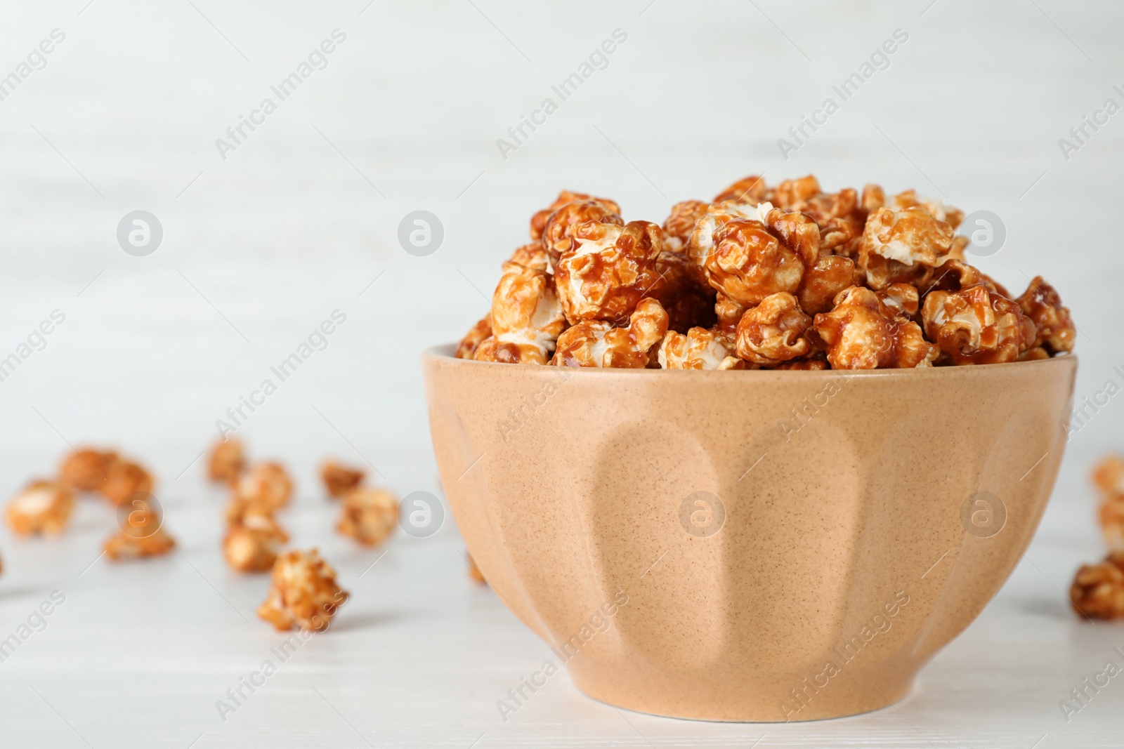 Photo of Bowl with tasty popcorn on white table. Space for text