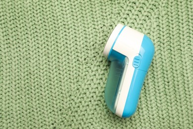 Photo of Modern fabric shaver for removing lint on green knitted cloth, top view