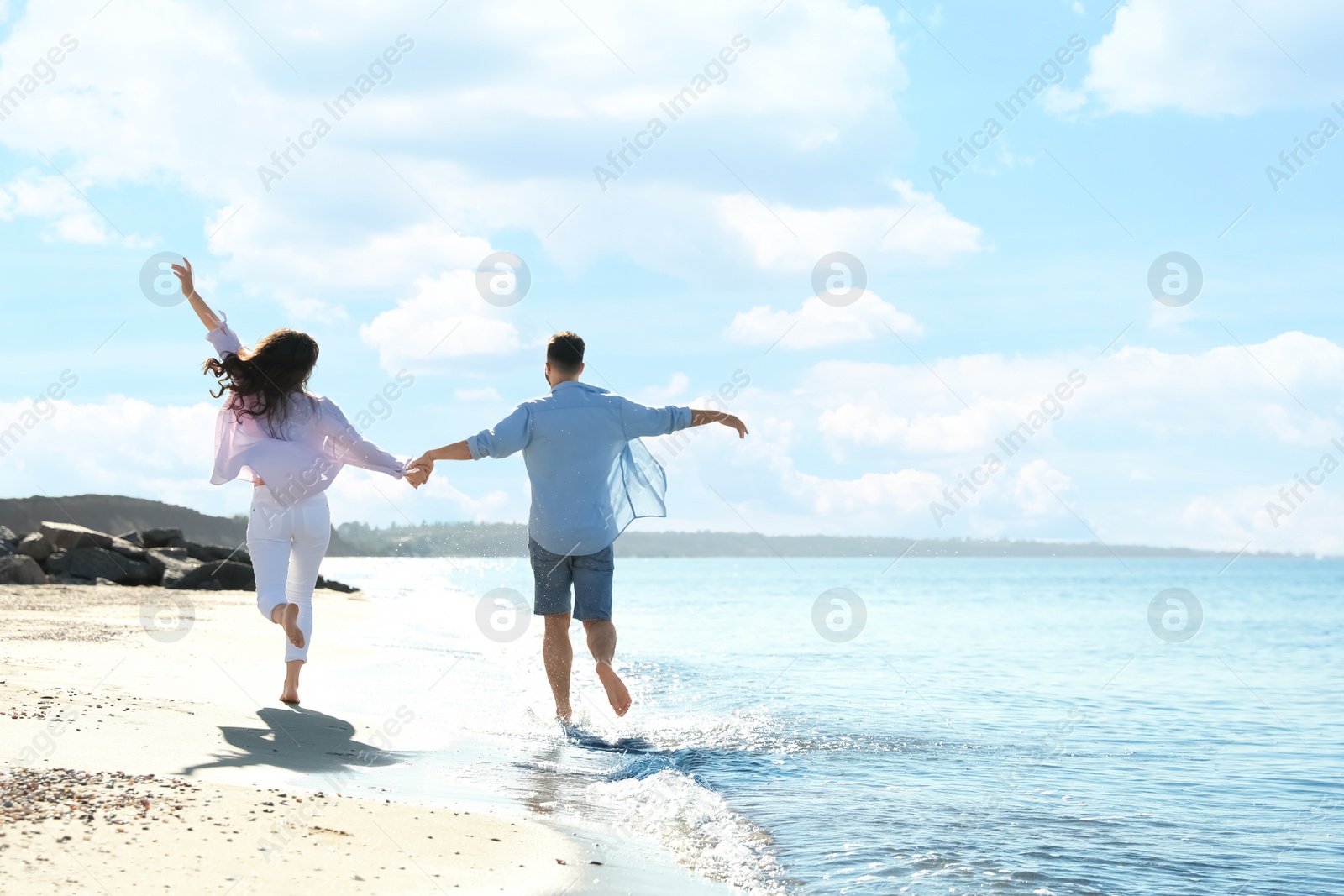 Photo of Young couple running on beach near sea. Honeymoon trip