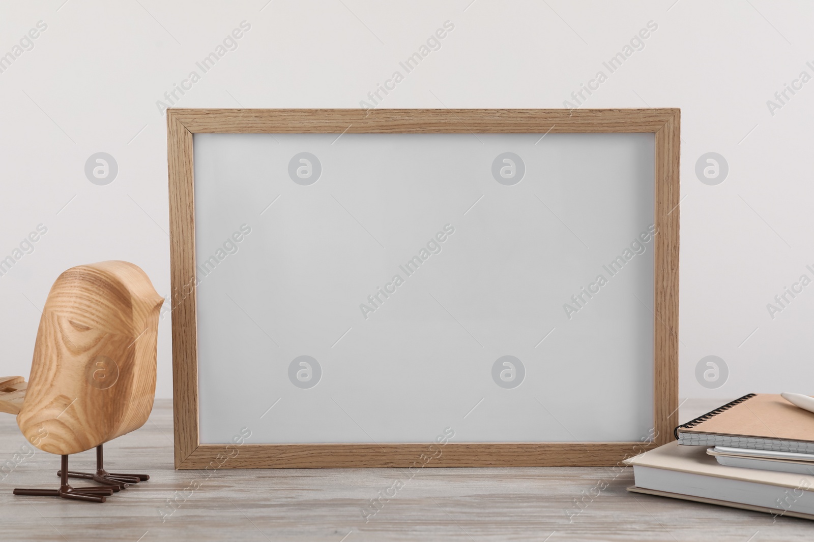 Photo of Blank photo frame, notebooks and decorative bird on wooden table