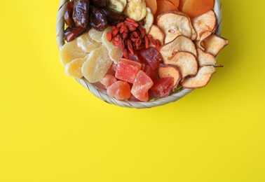 Photo of Wicker basket with different dried fruits on yellow background, top view. Space for text