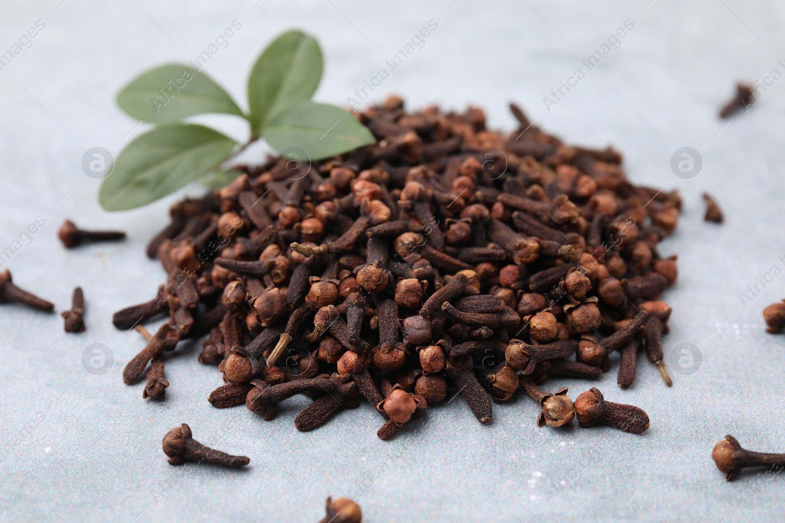 Photo of Pile of aromatic dried clove buds and leaves on grey table, closeup