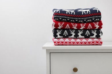 Photo of Different folded Christmas sweaters on chest of drawers against light background. Space for text