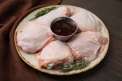 Plate with fresh marinade, raw chicken and rosemary on wooden table, closeup