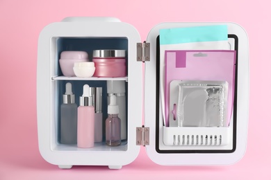 Photo of Open cosmetic refrigerator with skin care products on pink background