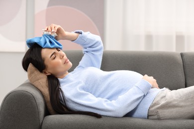 Photo of Pregnant woman with cold pack suffering from headache on sofa at home