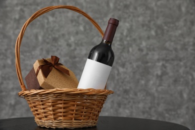 Photo of Wicker basket with bottle of wine and gift box on table. Space for design