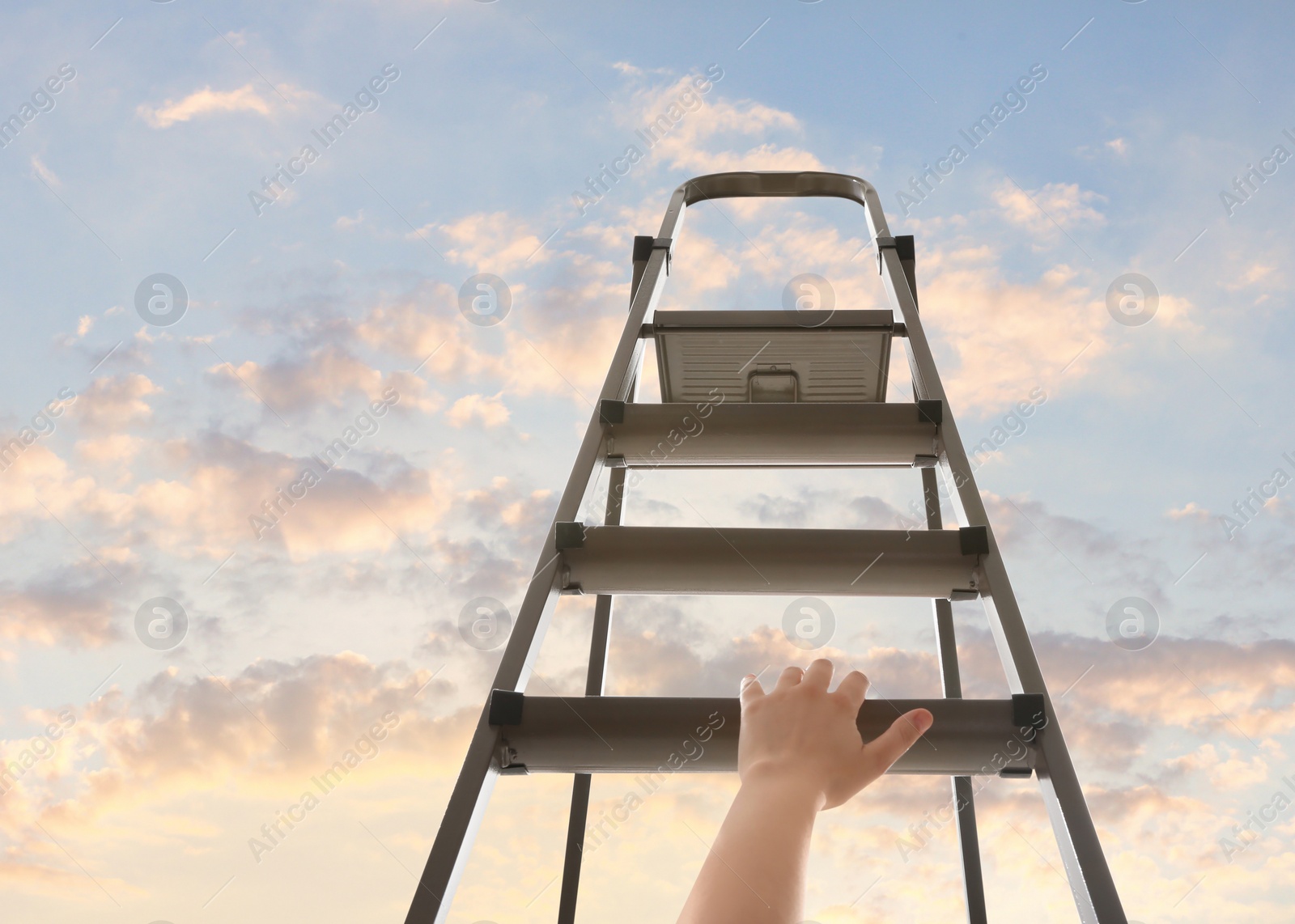 Image of Woman climbing up stepladder against sky with clouds, closeup