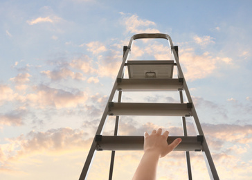 Image of Woman climbing up stepladder against sky with clouds, closeup