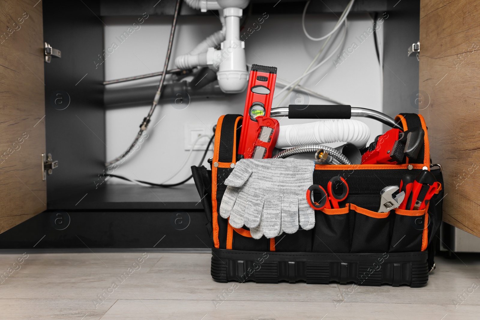 Photo of Plumber's tool bag on floor under kitchen sink