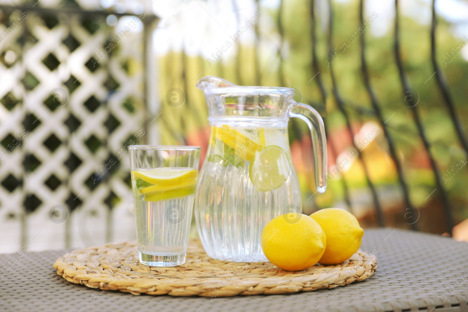 Photo of Glass and jug of water with lemons on table outdoors