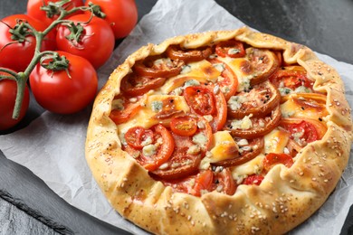 Photo of Tasty galette with tomato and cheese (Caprese galette) on dark table, closeup