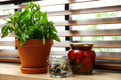 Photo of Green basil, pickled tomatoes and spices on window sill indoors