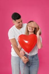 Photo of Man surprising his girlfriend with heart shaped balloon on pink background. Valentine's day celebration